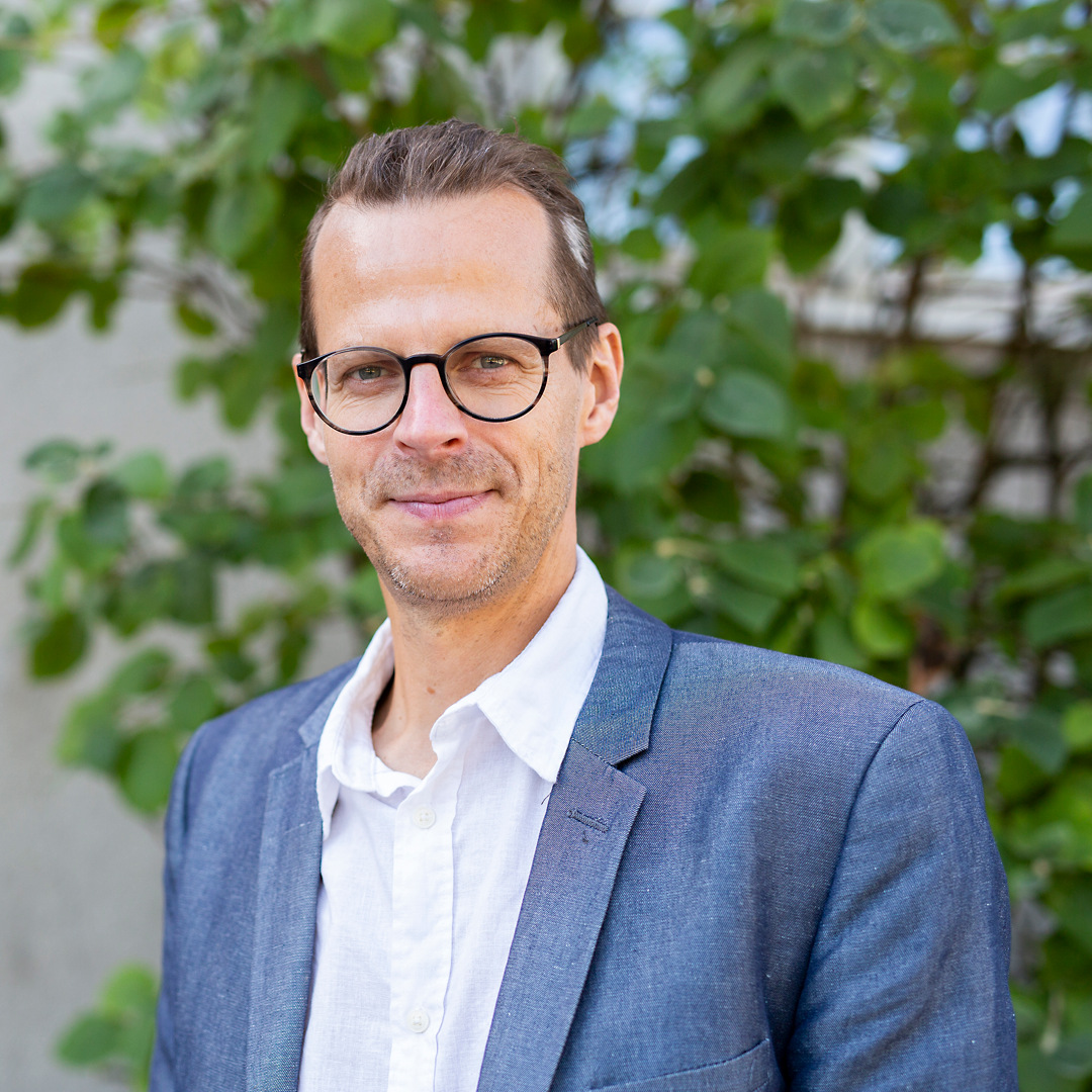 Sommarbild och porträtt av Martin Nihlgård som står framför ett grönt träd.