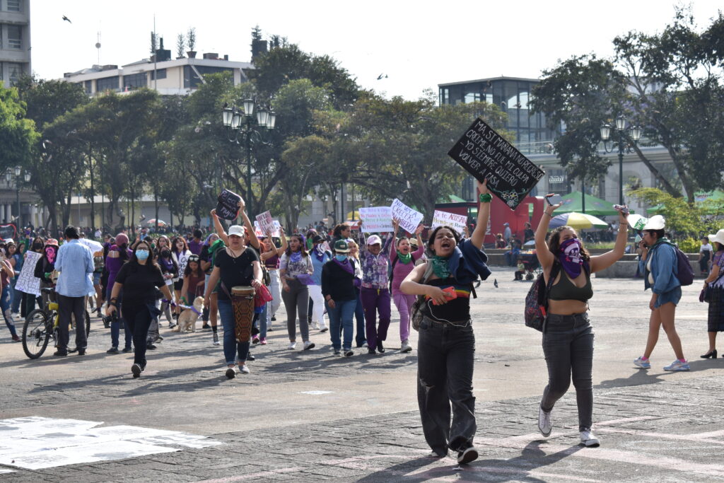 Demonstration med kvinnor som bär skyltar och ropar slagord på ett torg.
